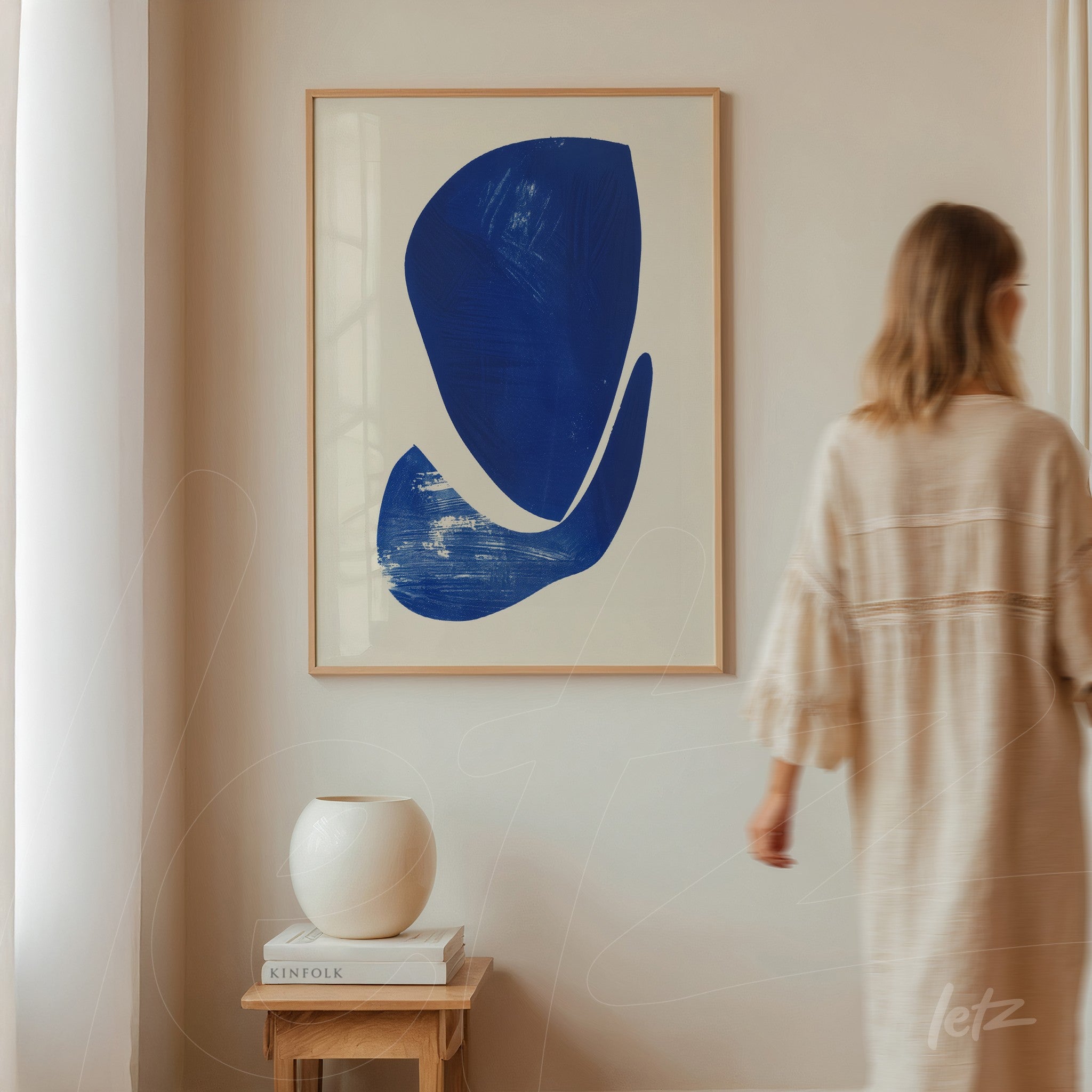 quadro em moldura clara com arte abstrata em azul sobre fundo branco, exposto em parede de ambiente minimalista