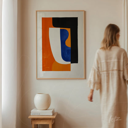 quadro abstrato com formas geométricas em preto, laranja e azul, em moldura clara, exposto em parede neutra ao lado de um vaso