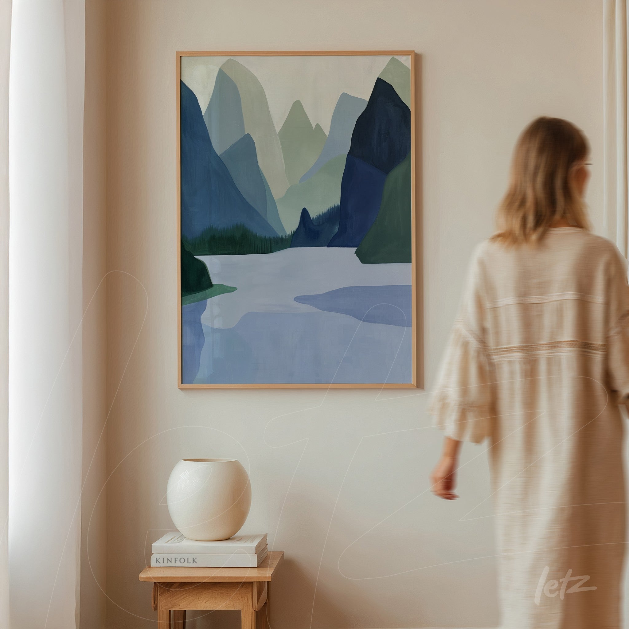 quadro decorativo com paisagem montanhosa em tons de azul e verde, moldura de madeira clara, exposto sobre parede clara
