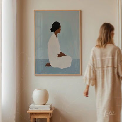 quadro em moldura clara com silhueta de mulher sentada em fundo azul suave, exibido em ambiente minimalista