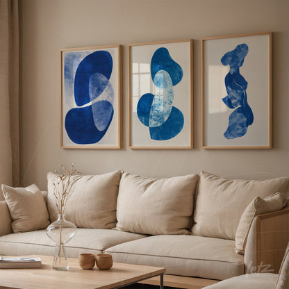 composição de três quadros decorativos com formas abstratas em tons de azul, molduras de madeira clara, exibidos sobre parede neutra em ambiente acolhedor