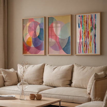 composição de três quadros decorativos com formas abstratas em cores suaves e molduras de madeira clara, exibidos sobre um sofá bege