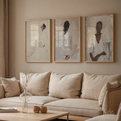 composição de três quadros decorativos com retratos femininos em moldura clara sobre parede neutra, exibidos acima de sofá em tonalidades suaves