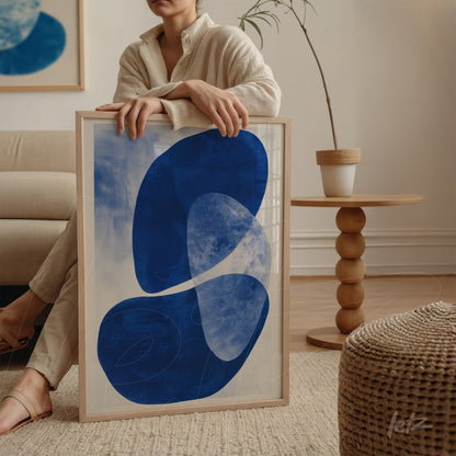 quadro em moldura clara com arte abstrata em tons de azul sobre fundo claro, apoiado em mesa redonda