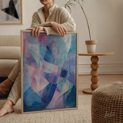 quadro abstrato em moldura de madeira clara com predominância de azul, rosa e lilás apoiado ao lado de uma poltrona em ambiente claro