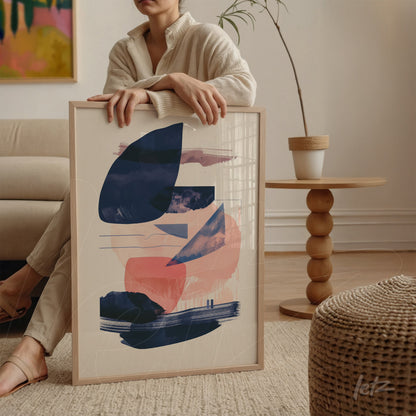 quadro decorativo com arte abstrata em cores azul marinho e rosa claro, em moldura de madeira clara, apoiado sobre mesa ao lado de planta