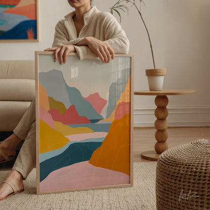 quadro com arte abstrata em tons de azul, rosa e laranja em moldura clara, apoiado em mesa ao lado de uma mulher