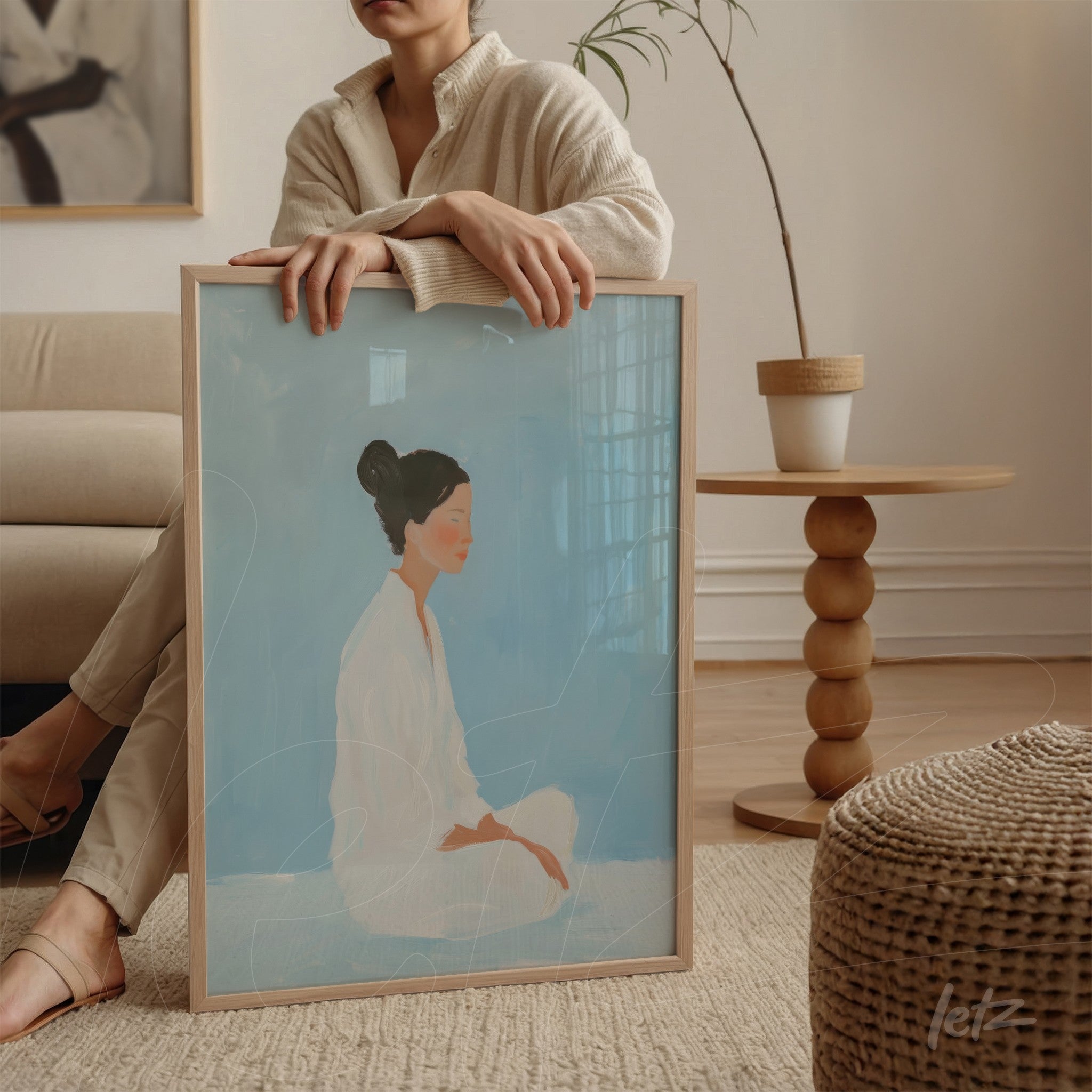 quadro com arte minimalista de mulher sentada com fundo azul, em moldura clara, apoiado sobre uma mesa redonda