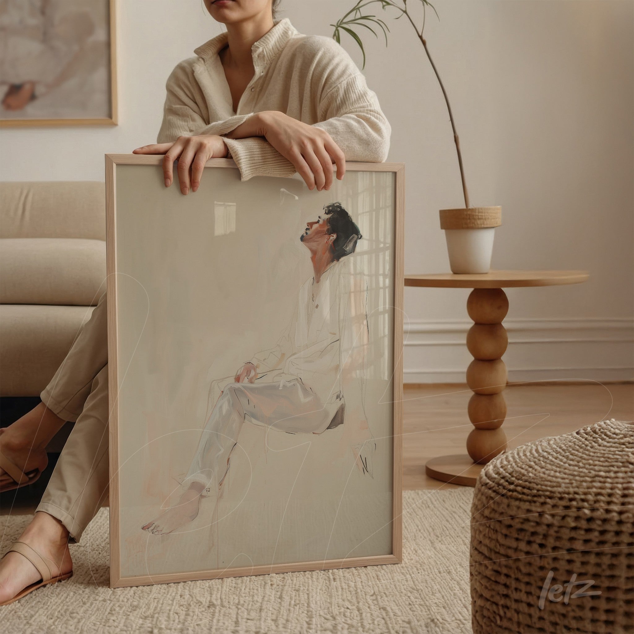 quadro com desenho minimalista de figura humana em moldura clara, apoiado na perna de uma mulher em sofá