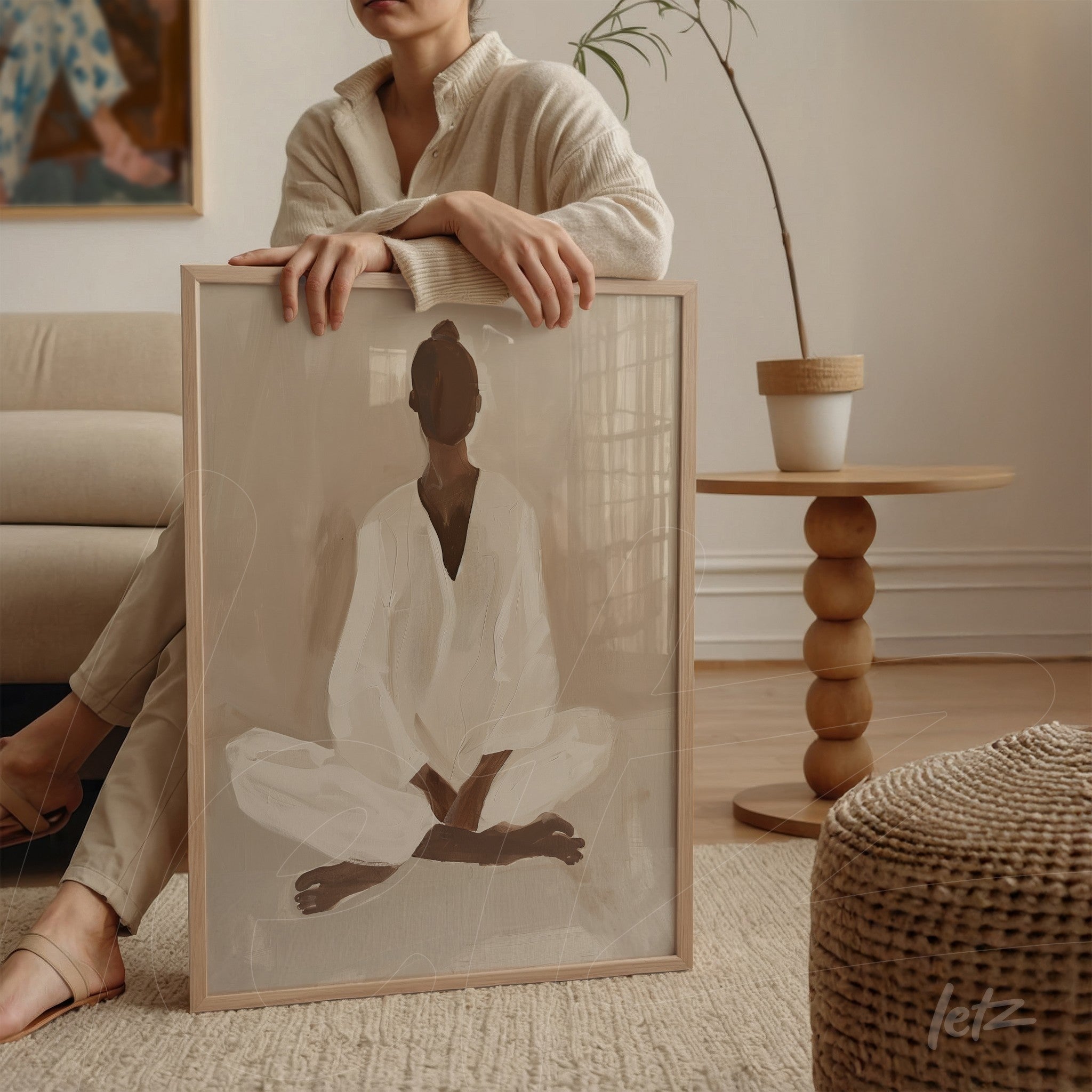 quadro com arte minimalista de figura meditando em moldura clara, apoiado em mesa ao lado de sofá
