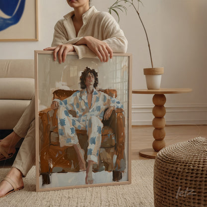 quadro com arte contemporânea retratando mulher relaxando em cadeira marrom, moldura clara e fundo neutro