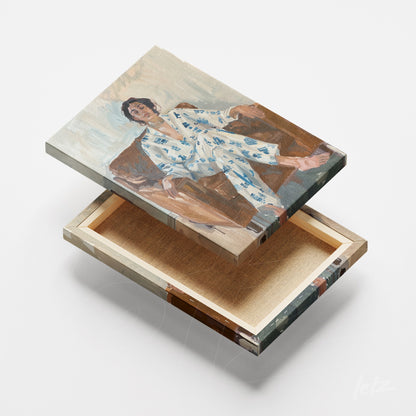 arte em tela de figura sentada em sofá vestindo pijama com estampa azul sobre base de madeira