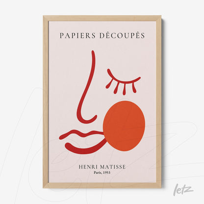 quadro em moldura clara com arte abstrata na forma de um rosto estilizado em fundo claro, apresentando traços vermelhos e uma forma circular laranja